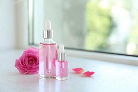 Bottles of rose essential oil and fresh flower on window sill, space for text Stock Photos