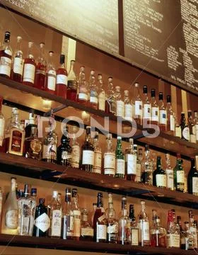 Bottles Of Spirits On A Glass Shelf Behind A Bar