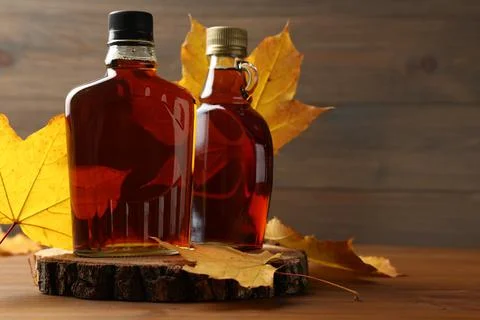 Bottles of tasty maple syrup and dry leaves on wooden table, space for text Stock Photos