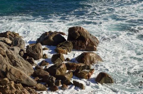 Bottom of a cliff while the rough sea impacts against the big dark rocks Stock Photos