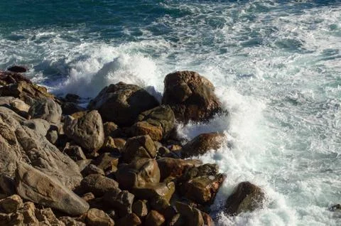 Bottom of a cliff while the rough sea impacts against the big dark rocks Stock Photos
