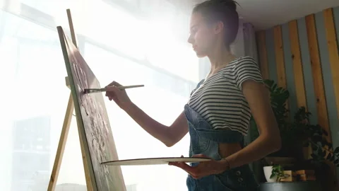Bottom side view of a pretty young woman artist paints an oil painting Stock Footage 111033007