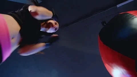 Bottom view, close-up cute brunette woman fulfills blows on punching bag in gym Stock Footage 93259678