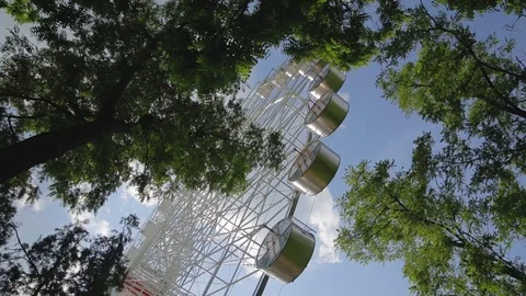 Bottom view ferris wheel slowly spins in circle through rustling tree foliage Stock-Footage 90731140