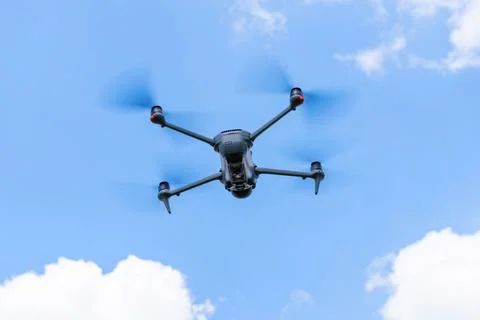 Bottom view of a flying drone with spinning propellers against blue sky and c 스톡 사진
