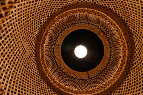 Bottom view of glowing light bulb inside wicker bamboo lampshade geometric .. Stock Photos