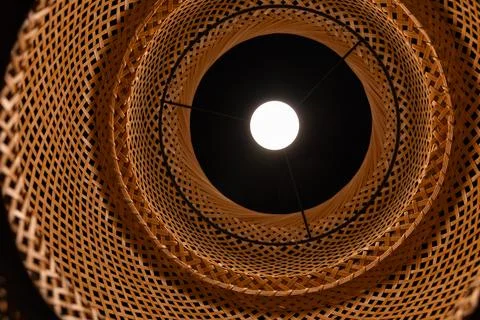 Bottom view of glowing light bulb inside wicker bamboo lampshade geometric .. Stock Photos