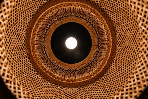 Bottom view of glowing light bulb inside wicker bamboo lampshade geometric .. Stock Photos