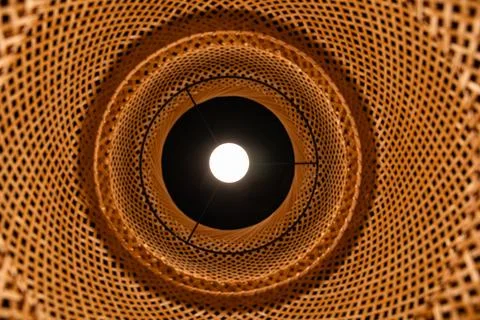 Bottom view of glowing light bulb inside wicker bamboo lampshade geometric .. Stock Photos