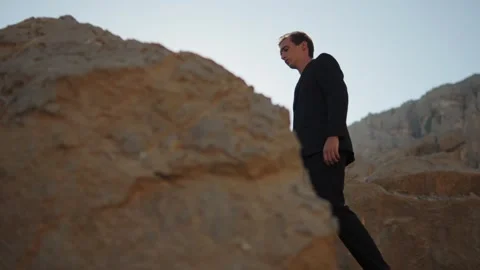 Bottom view of a guy model in a suit walking on rocks in the mountains. Stock Footage 305588948