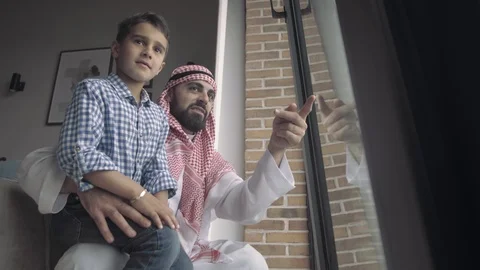 Bottom view handsome Arab man in traditional dress holds his son Stock Footage 113748817