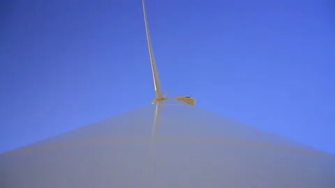 Bottom view of a large wind turbine spinning against a clear blue sky producing Stock Footage 222417245