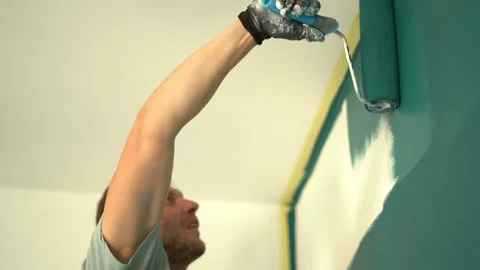 Bottom view, low angle shot. A young man paints a wall with a paint roller from Stock Footage 169601525