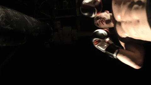 Bottom view of a man boxer beats a punching bag while training in a dark gym Stock Footage 112946480