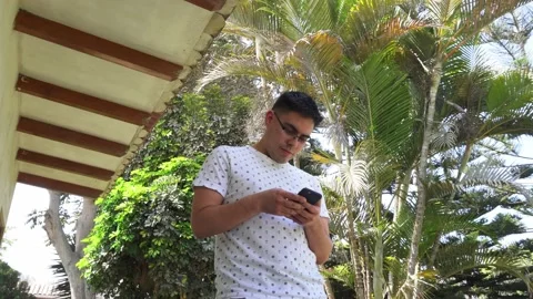 Bottom view of a man with glasses looking at his cell phone next to palm trees Stock Footage 161936975