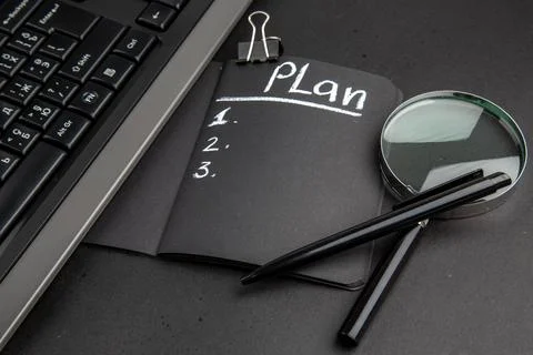 Bottom view plan written on black notepad lupa keyboard binder clip pen on .. 写真素材