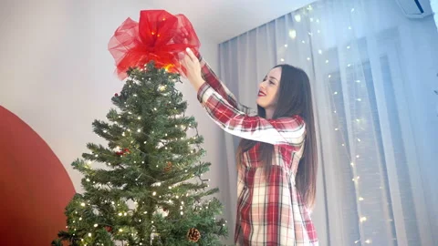 Bottom view shot of happy smiling woman tying red big bow on Christmas tree Stock Footage 250283964