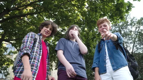 Bottom view of three schoolboys pointing down and laughing at camera. Aggressive Stock-Footage 143381556