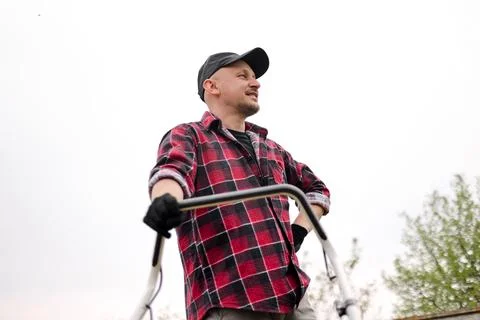 Bottom view of tired man makes a short break while cutting grass with a lawn Stock Photos