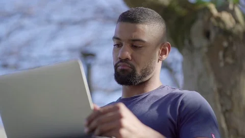 Bottom view of young man in park opening laptop, thinking 스톡 동영상 105432144