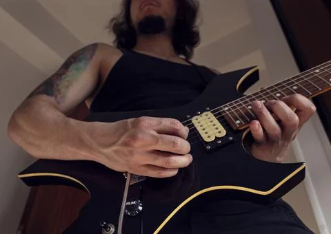 Bottom view of a young man playing a black and yellow electric guitar at indoor Stock-Fotos