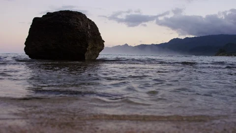 Boulder in the ocean gets hit by waves as sun sets Stock Footage 105936232