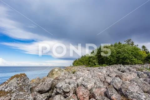 Boulders, forest, shore, evening light, sunset, clouds, blue sky and rainbow Stock Photos