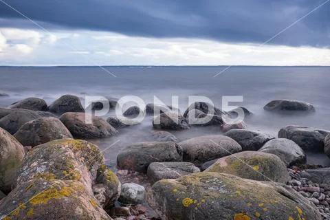Boulders, forest, shore, evening light, sunset, clouds, blue sky and rainbow Stock Photos