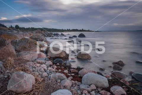 Boulders, forest, shore, evening light, sunset, clouds, blue sky and rainbow Stock Photos