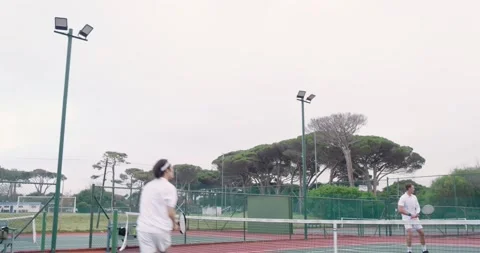 Bouncing ball prompting two male tennis players serving and volleying on red Stock Footage 340881159