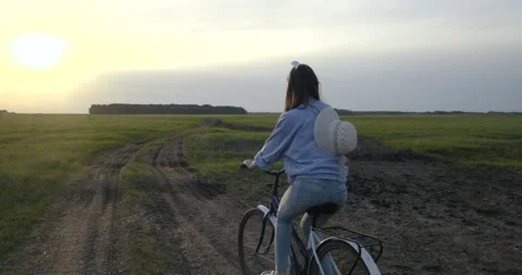 Boundless Village Field in Sunset Rays. Along Country Road Rides Girl on Bicycle Stock Footage 132471237