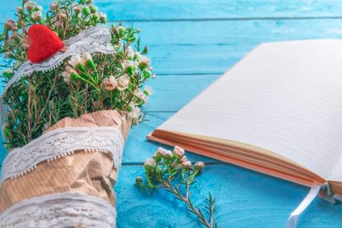 Bouquet of flowers and an empty notebook on a blue table Stock Photos
