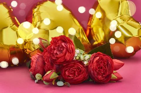 A bouquet of red roses against the background of golden balloons in the form of Stock Photos