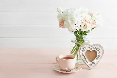 Bouquet of roses, eustomas and hydrangeas on table. Cup of tea and photo fram Stock Photos