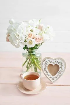 Bouquet of roses, eustomas and hydrangeas on table. Cup of tea and photo fram Stock Photos