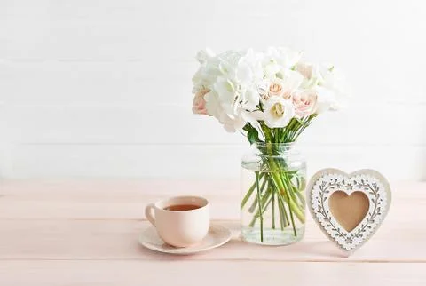 Bouquet of roses, eustomas and hydrangeas on table. Cup of tea and photo fram Stock Photos