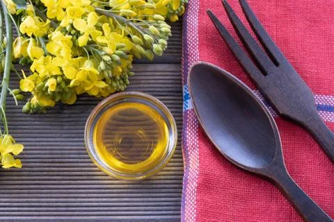 Bouquet of spring rape next to a cup with rapeseed oil and wooden cutlery on Stock Photos