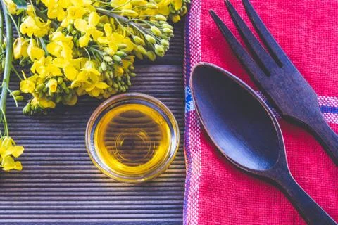 Bouquet of spring rape next to a cup with rapeseed oil and wooden cutlery Stock Photos