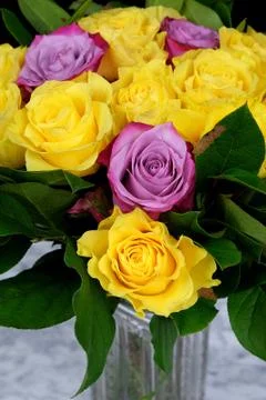 Bouquet of yellow roses with three purple in the glass vase on the marble tab Stock Photos
