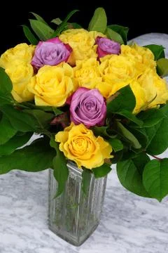 Bouquet of yellow roses with three purple in the glass vase on the marble tab Stock Photos