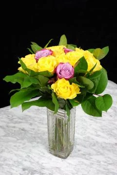 Bouquet of yellow roses with three purple in the glass vase on the marble tab Stock Photos