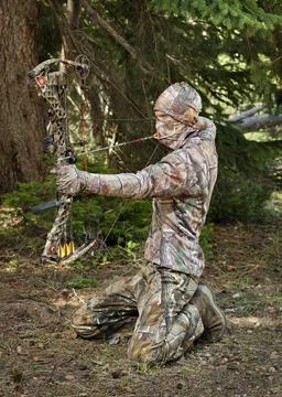 Bow hunter pulling compound bow in trees Stock Photos