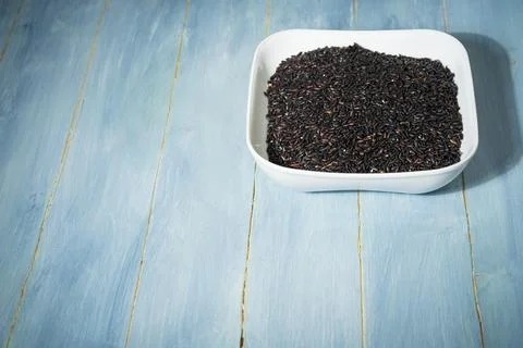 A bowl of black raw rice is placed on a yellow table 库存照片