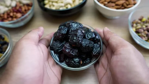 Bowl of Dried Dates with Nuts in Background, Hands holding a bowl of dark d.. Stock Footage 318578630