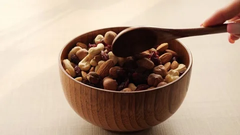 Bowl filled with mix assorted nuts and dried fruits sits on table, as spoon Stock Footage 268210849