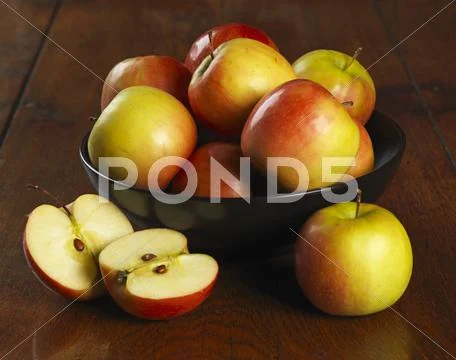 A Bowl Of Fresh Apples With One In Front Cut In Half