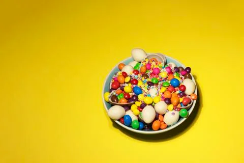 A bowl full of different chocolates and jellies on a yellow background Stock Photos