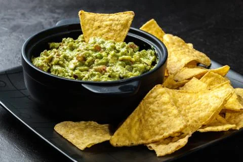 Bowl of guacamole with corn chips on a black table Stock Photos