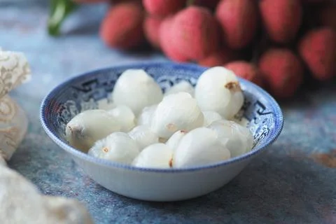 Bowl of lychee fruit on a table with additional lychee in the background Stock Photos