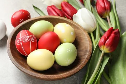 Bowl with painted Easter eggs and spring flowers on light background Stock Photos